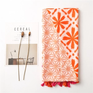 Detail view of cotton-linen scarf with orange floral prints and fringe edges beside a magazine
