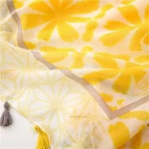 Macro detail of yellow floral scarf fabric showing fine texture and delicate fringe trim