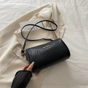 Classic black woven cylinder shoulder bag with golden fashion logo on beige suit