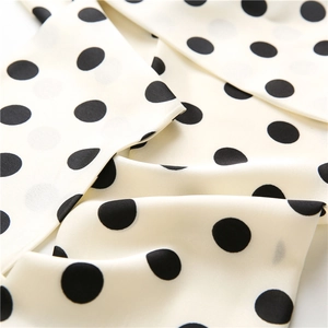 Detail of silk-like cream fabric with black polka dots showing soft texture and drape