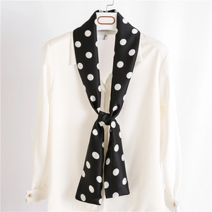 Elegant black skinny scarf with white polka dots tied on a white shirt collar