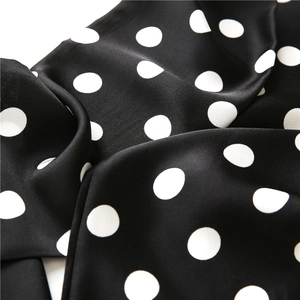 Close-up of silky black scarf with white polka dots showing smooth drape and texture