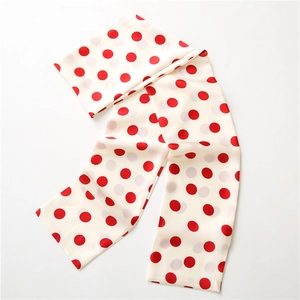 Polka dot long skinny silk scarf in cream and red, stylishly draped on a plain white background