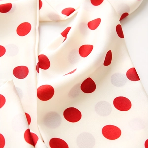 Detailed close-up of soft satin scarf with elegant red and grey polka dots on beige