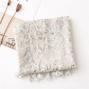 Détail de l'imprimé serpent argenté sur écharpe en coton beige avec pompons blancs