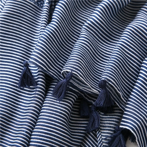 Détail d'une écharpe rayée bleu et blanc en coton et lin avec d'élégants pompons bleus