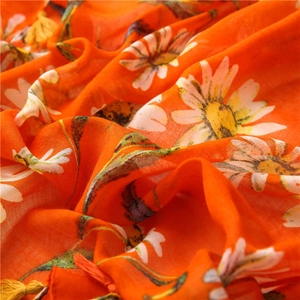 Detail of vibrant orange scarf with white daisy patterns and decorative yellow tassels