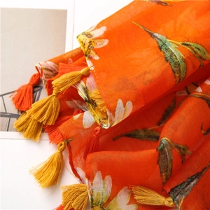 Detail of orange floral print scarf with intricate yellow tassels and linen texture