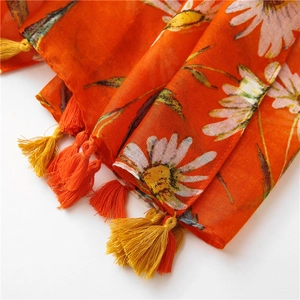 Detail of orange cotton-linen scarf featuring white daisy prints and fringe tassels