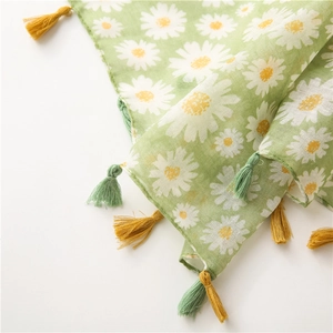Détail d'une écharpe en coton vert avec motif marguerites et bordures à pompons