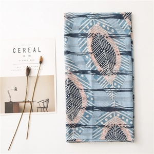 Mise à plat d'une écharpe en lin bleu clair avec motifs plumes à côté d'un magazine