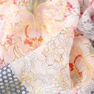 Close-up of lightweight floral scarf with gold foil accents on soft pink fabric