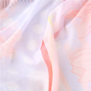 Close-up of lightweight chiffon fabric with white polka dots and soft pink floral prints