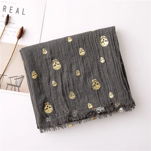 Detail of grey linen scarf with gold skull prints and frayed edge tassels on a white background
