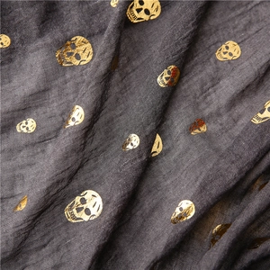 Macro detail of dark grey scarf showing golden skull foil print on pleated linen fabric