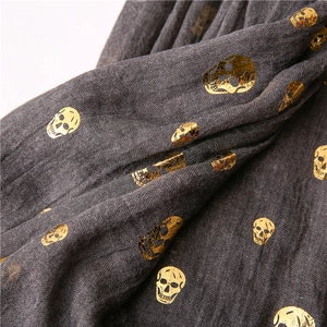 Close-up of dark grey cotton linen scarf with gold foil skull prints in punk style