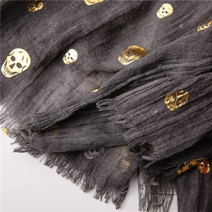 Detailed close-up of dark grey cotton linen scarf with gold foil skull prints and frayed edges