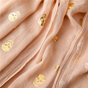 Detail of light pink scarf fabric with golden skull pattern and breathable texture