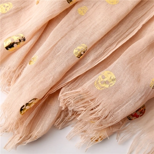 Detail of gold foil skull pattern on beige cotton linen scarf with frayed tassel edges