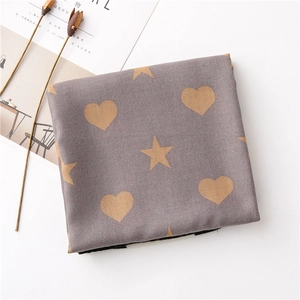 Detail of greyish-purple fabric scarf with gold heart and star prints on white background