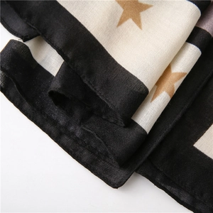 Detail of soft scarf featuring black border with golden star pattern on beige fabric