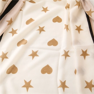 Detail of cream scarf featuring gold stars, hearts, and striped contrast edges