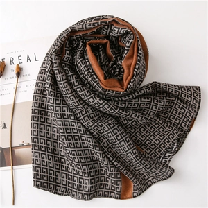 Dual-sided geometric cashmere scarf with orange and grey patterns on a white table