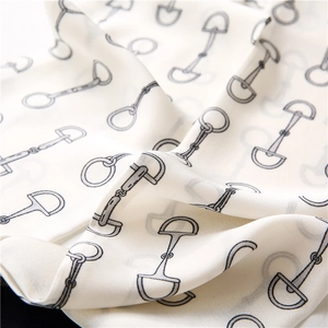 Detail of cream silk scarf featuring a classic black horsebit pattern and smooth texture