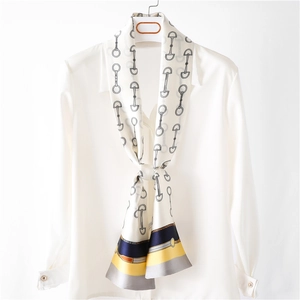 Detailed close-up of skinny silk scarf with classic horsebit chain pattern and contrast hem