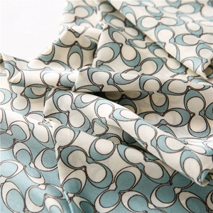Macro view of blue and beige silk scarf featuring repeating C-shaped geometric patterns