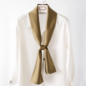 Gros plan sur un foulard en soie marron doré noué sur un col de chemise blanche