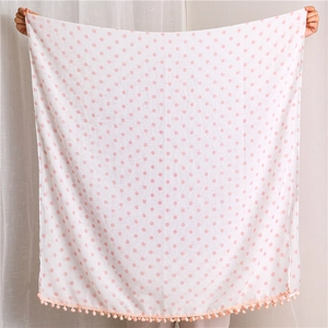 Detail of white scarf with pink polka dots and soft pom-pom trim held by hands