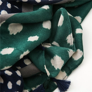 Vue détaillée de l'écharpe vert foncé avec taches de léopard blanches et pompon à franges