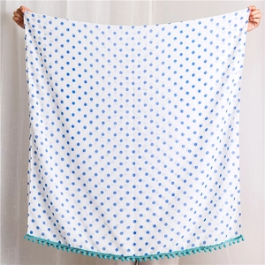 Detailed view of white polka dot bath towel with blue dots and green pompom fringe edge