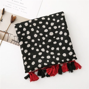 Détail d'une écharpe noire à pois blancs avec des pompons rouges et noirs aux bords