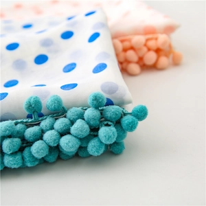 Detailed macro view of white chiffon scarf with blue polka dots and soft pom-pom trim