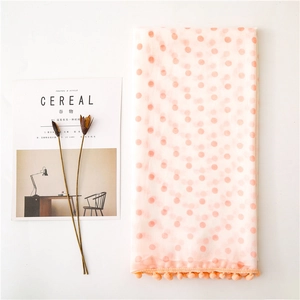 Flat lay of pink chiffon scarf with orange polka dots and pom-pom tassel fringe detail