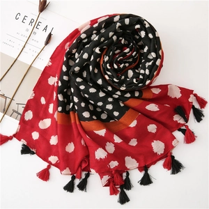 Détail d'une écharpe rouge et noire à pois avec glands et accessoires rustiques