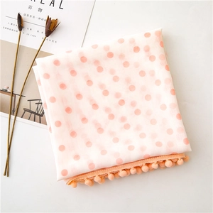 Detail of pink polka dot scarf with delicate pom-pom fringe trim on a white background