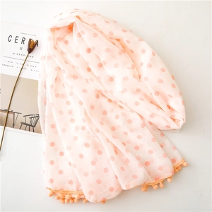 Detail of pink-orange polka dot scarf with pom-pom fringe edges and soft texture