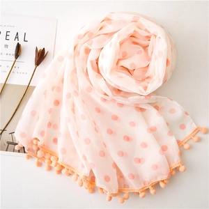 Detail of light pink polka dot scarf with orange pom-poms and soft airy texture