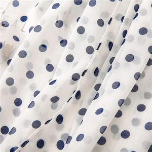 Lightweight white polka dot chiffon fabric with dark blue dots and natural drape detail