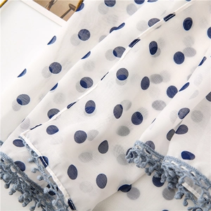 Macro detail of lightweight white fabric with navy polka dots and blue crochet ball fringe