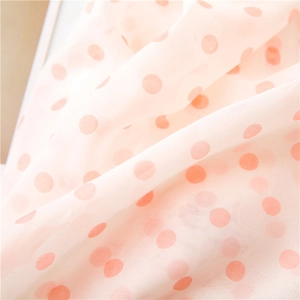Macro shot of light pink chiffon fabric with orange polka dots and soft pleated folds