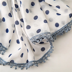Close-up of white fabric with blue polka dots and delicate lace tassel fringe detail
