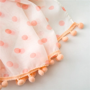 Close-up of lightweight off-white scarf fabric with orange dots and pom-pom trim detail