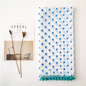 Flat lay of a white sheer scarf with blue polka dots and teal pompom fringe detail
