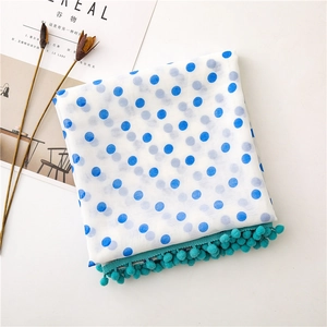 Detail of blue polka dot scarf with turquoise pom-pom trim on a white surface