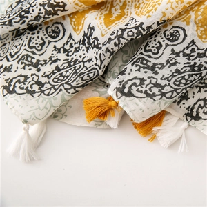 Detail of paisley print cotton linen shawl with yellow and white tassels on a white background