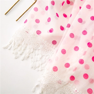 Detail of pink polka dot fabric with intricate white floral lace trim and fringe edge
